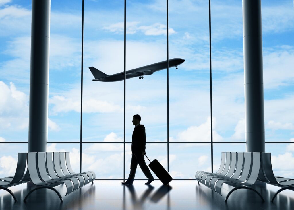 A man at an airport pulling luggage with an airplane taking off out the window